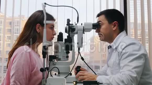 眼科治疗一位医生用一台特殊的机器检查年轻女性视力一个宽敞的橱柜配有一台特殊的机器视频的预览图