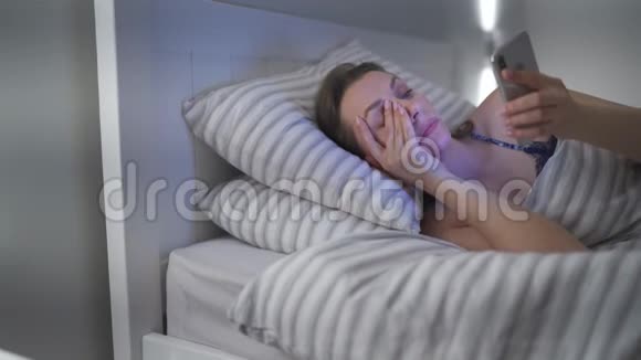 女人躺在床上用智能手机她揉眼睛因为她又累又困增加的概念视频的预览图