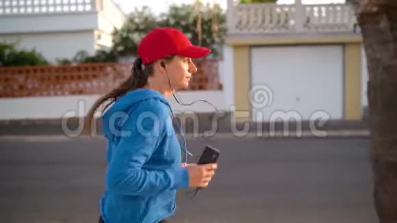 带着耳机和智能手机的女人在街上跑健康的积极生活方式慢动作侧视图视频的预览图