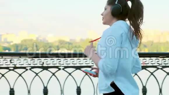 一个穿着白色毛衣戴耳机的漂亮女孩在早晨慢镜头拍摄侧景视频的预览图