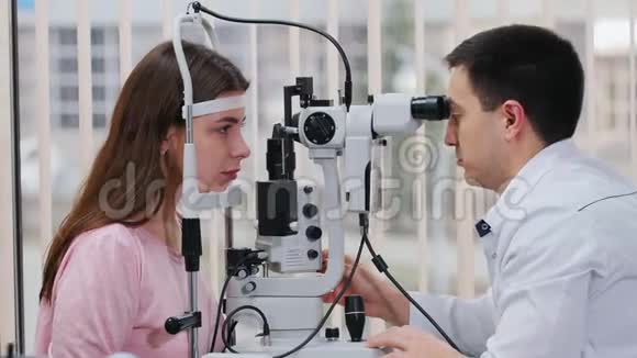 眼科治疗一位医生用一台特殊的机器检查年轻女性视力一个宽敞的橱柜配有一台特殊的机器视频的预览图