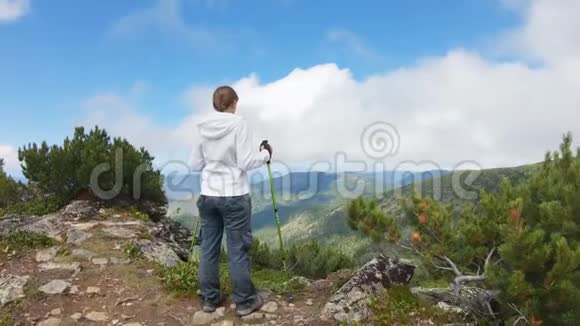 带着跋涉杆的女人站在山顶凝视着风景视频的预览图