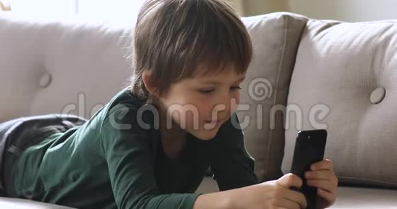 好奇可爱的小学生独自拿着智能手机在家看视频视频的预览图