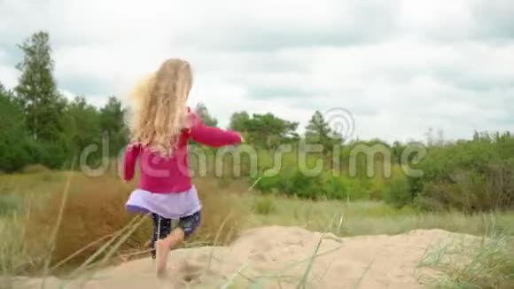 五岁的金发女孩穿着粉色衬衫赤脚走在沙丘上视频的预览图