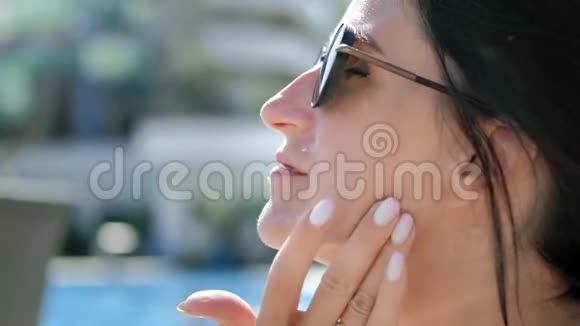 在日光浴期间戴太阳镜的微笑放松的女士用防晒霜做特写视频的预览图