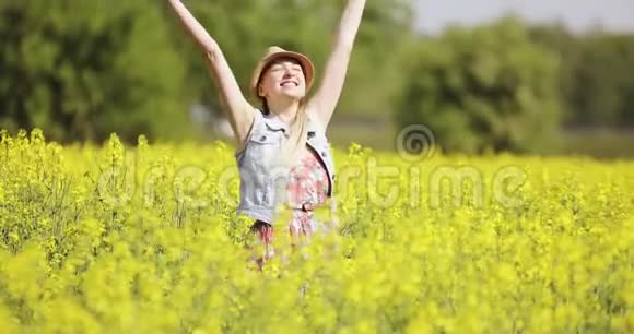 快乐的白种人女人穿着一件漂亮的连衣裙在一片盛开的黄色田野里愉快地跳舞视频的预览图