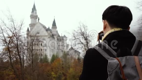 男性亚洲游客背包和相机站立欣赏中世纪的Neuschwanstein城堡视频的预览图