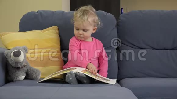 小好奇的女孩看书玩具熊坐在蓝色的沙发上视频的预览图