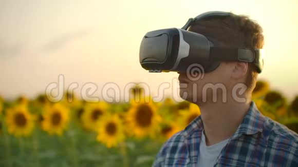 一个现代农民在一个有向日葵的田野里用虚拟现实眼镜和手势来控制浇水图和视频的预览图