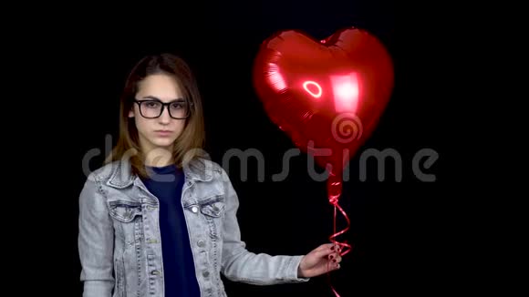 伤心的年轻女子松开了心形气球一个悲伤的女人站在黑色的背景上带着氦球情人节视频的预览图