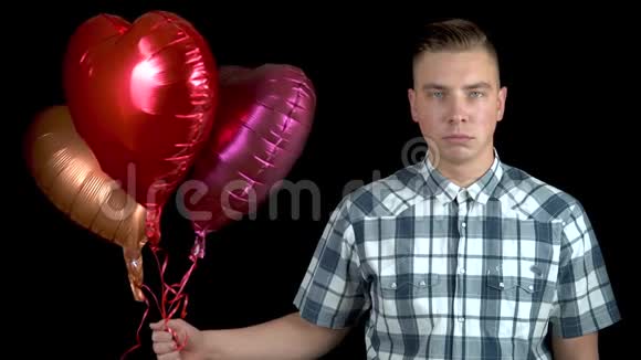 悲伤的年轻人放下心形气球一个悲伤的人站在黑色的背景上带着氦球情人节视频的预览图