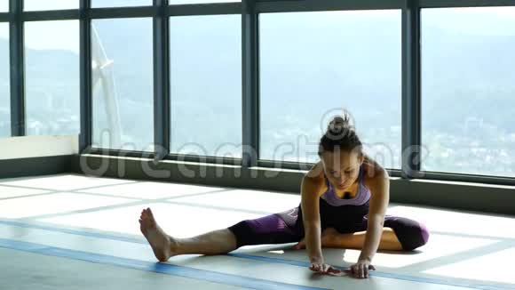 在瑜伽室的大窗户附近做伸展运动的女人视频的预览图