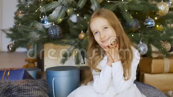 可爱的金发女孩在圣诞树旁的礼物盒里思考礼物快乐的童年和圣诞节视频的预览图