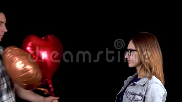 一个年轻人给一个年轻的女人心形气球男人和女人在黑色背景上接吻情人节是视频的预览图