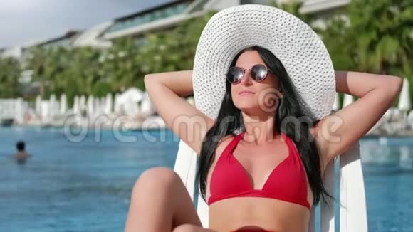 时尚旅游女性穿红色泳衣在豪华酒店的甲板椅上日光浴中型特写视频的预览图