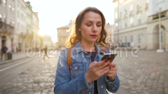 日落时分女人用智能手机走在老街上传播社交网络的概念慢动作视频的预览图