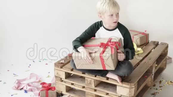 一个金发男孩坐在托盘上手里拿着一件包装精美的礼物视频的预览图
