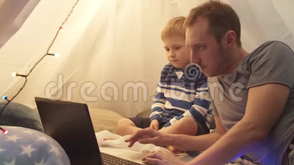 小男孩和他的父亲在家里孩子们的帐篷里玩和看动画片快乐的白种人小孩在游戏室视频的预览图