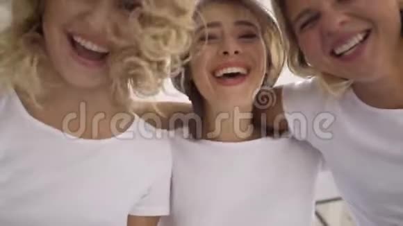 三个可爱的微笑迷人的女人穿着白色t恤看着相机拥抱在一起的肖像快乐视频的预览图