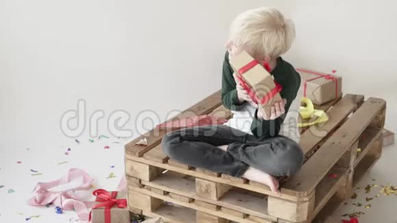 金发男孩坐在木制托盘上手里拿着礼物视频的预览图