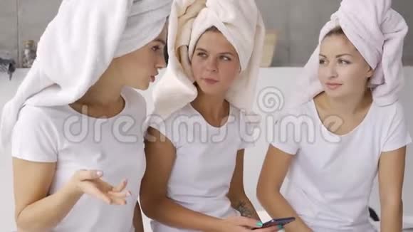 三个积极的女朋友穿着白色的t恤头上有毛巾在家里在浴室里聊天睡衣派对视频的预览图