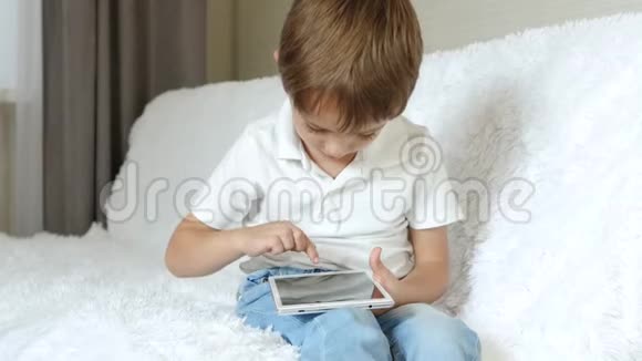 男孩热情地玩着一块平板电脑坐在沙发上视频的预览图