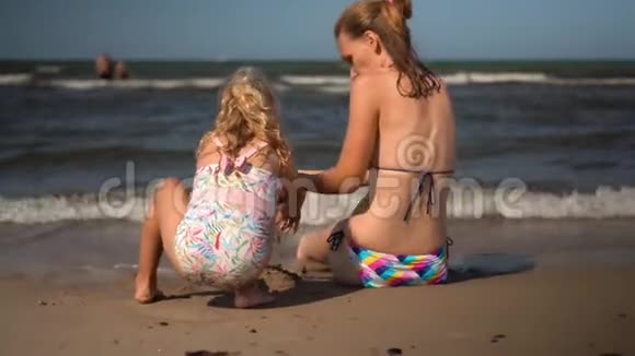 可爱的母亲和小女儿在潮湿的沙滩上建造城堡视频的预览图