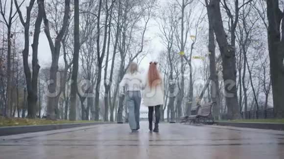 镜头跟随年轻的白人男子长发和红头发的女人走在小巷在秋季城市公园快乐视频的预览图