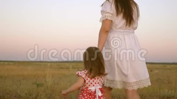 宝贝牵着妈妈手一个幸福的家庭在晚上走出城镇妈妈和她的小女儿一起走在田野上视频的预览图