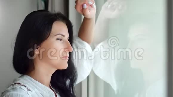 美丽的忧郁的黑发女人穿着白色衬衫看着窗外的特写视频的预览图