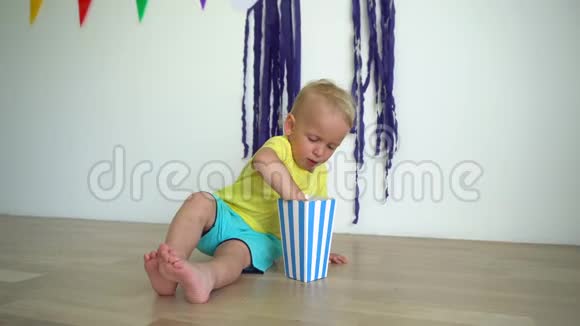 坐在木地板上的纸盒子里吃爆米花的小男孩视频的预览图