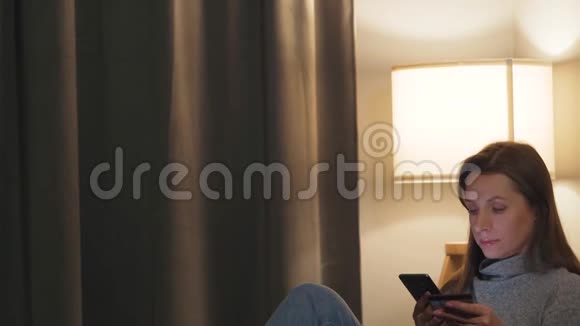 女人躺在舒适的房间里的沙发上用信用卡和智能手机在线购买网上在线视频的预览图