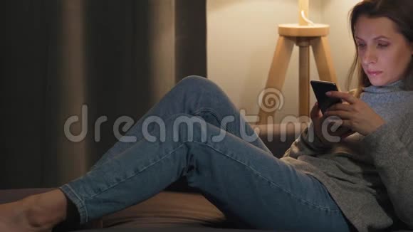 女人躺在舒适的房间里晚上用智能手机上网放松和视频的预览图