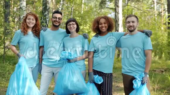 快乐的青年志愿者带着垃圾袋站在森林里拥抱微笑视频的预览图