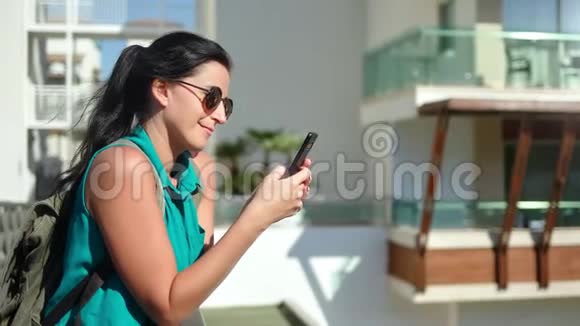 旅游阳光女孩背包微笑聊天使用智能手机露台享受假期视频的预览图