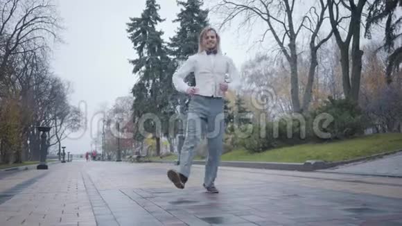 年轻开朗的白种人男孩穿着优雅的白色衬衫背心格子蝴蝶结领带在城市公园跳舞有趣的白人视频的预览图