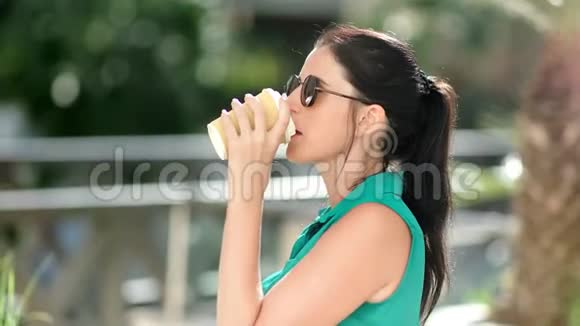 在阳光明媚的夏日公园特写镜头中微笑的休闲年轻女士喝着咖啡纸杯欣赏大自然视频的预览图