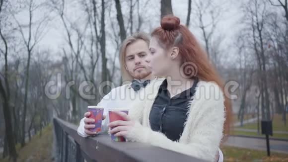 侧面观看迷人的白种人女孩与红色头发与时尚男孩与长发年轻的情侣在秋天约会视频的预览图