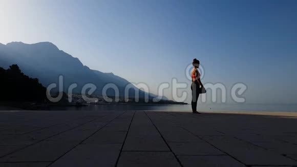 运动女孩在风景优美的海景中展开瑜伽垫的剪影视频的预览图