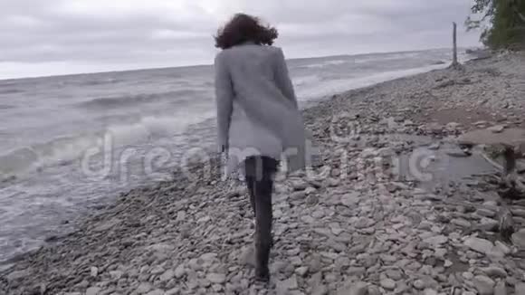 一个穿着灰色外套的女孩沿着海边的石头散步视频的预览图