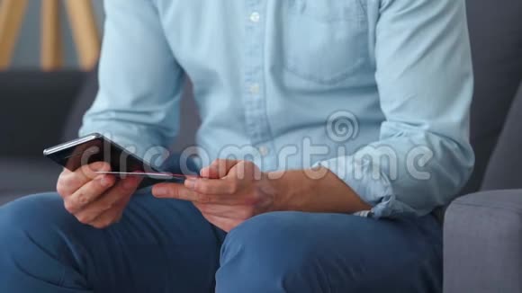 穿着正式服装的男人坐在沙发上从几张信用卡中选择然后把它的号码输入智能手机支付视频的预览图