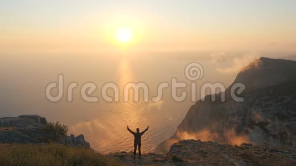 一位年轻女子站在悬崖边从高处眺望大海上美丽的戏剧性日落视频的预览图