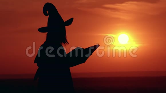 穿着奇装异服戴帽子的女孩女巫施咒施咒的日出景色视频的预览图