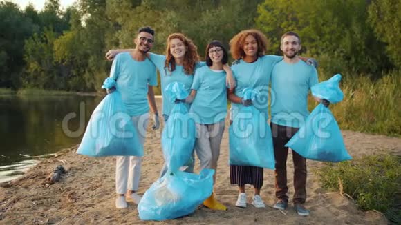 多种族的志愿者在清洁的湖面上拥抱微笑的垃圾袋视频的预览图