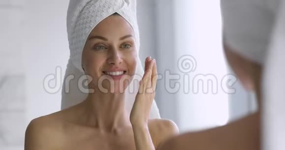 有趣的女人在脸上涂上护肤霜照镜子视频的预览图
