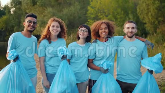 欢乐的朋友环保活动人士手里拿着垃圾袋站在河岸上拥抱视频的预览图