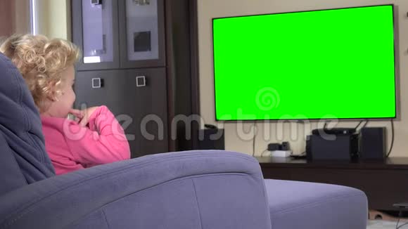 女孩坐下来在柔软的沙发上看电视电视背景绿色4K视频的预览图