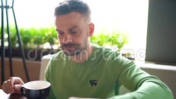 留着卷曲胡子的大胡子男人在咖啡馆里吃巧克力喝咖啡视频的预览图
