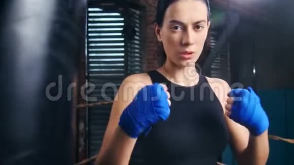 咄咄逼人的女踢球手脸上的汗滴在蓝色包裹的手在黑暗的健身房摆姿势视频的预览图