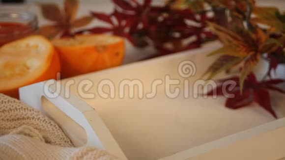 女人的手把碗和南瓜汤放在白色的托盘上背景上有秋叶和南瓜视频的预览图
